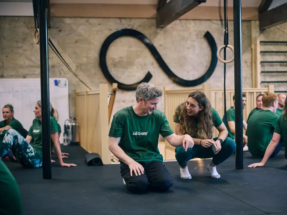 A CaliUnity coach crouching beside a member on the gym floor, both smiling